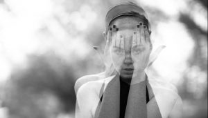 Double exposure image of young woman with hands over her eyes and also looking at the camera